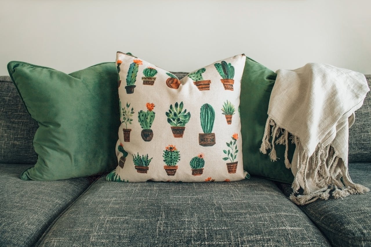 A modern living room with green cushions, cactus pillow, and cozy throw blanket on a sofa.